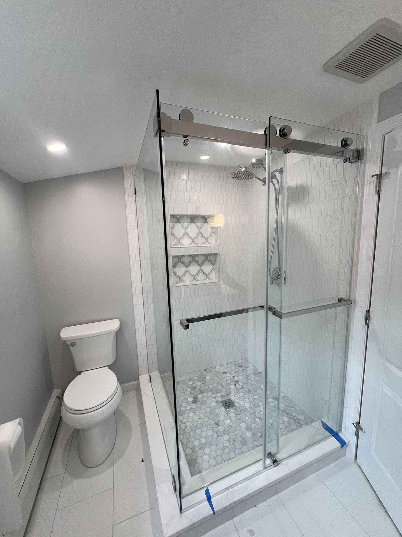A bathroom with a frameless glass shower, picket wall tile and a marble hexagon mosaic floor.