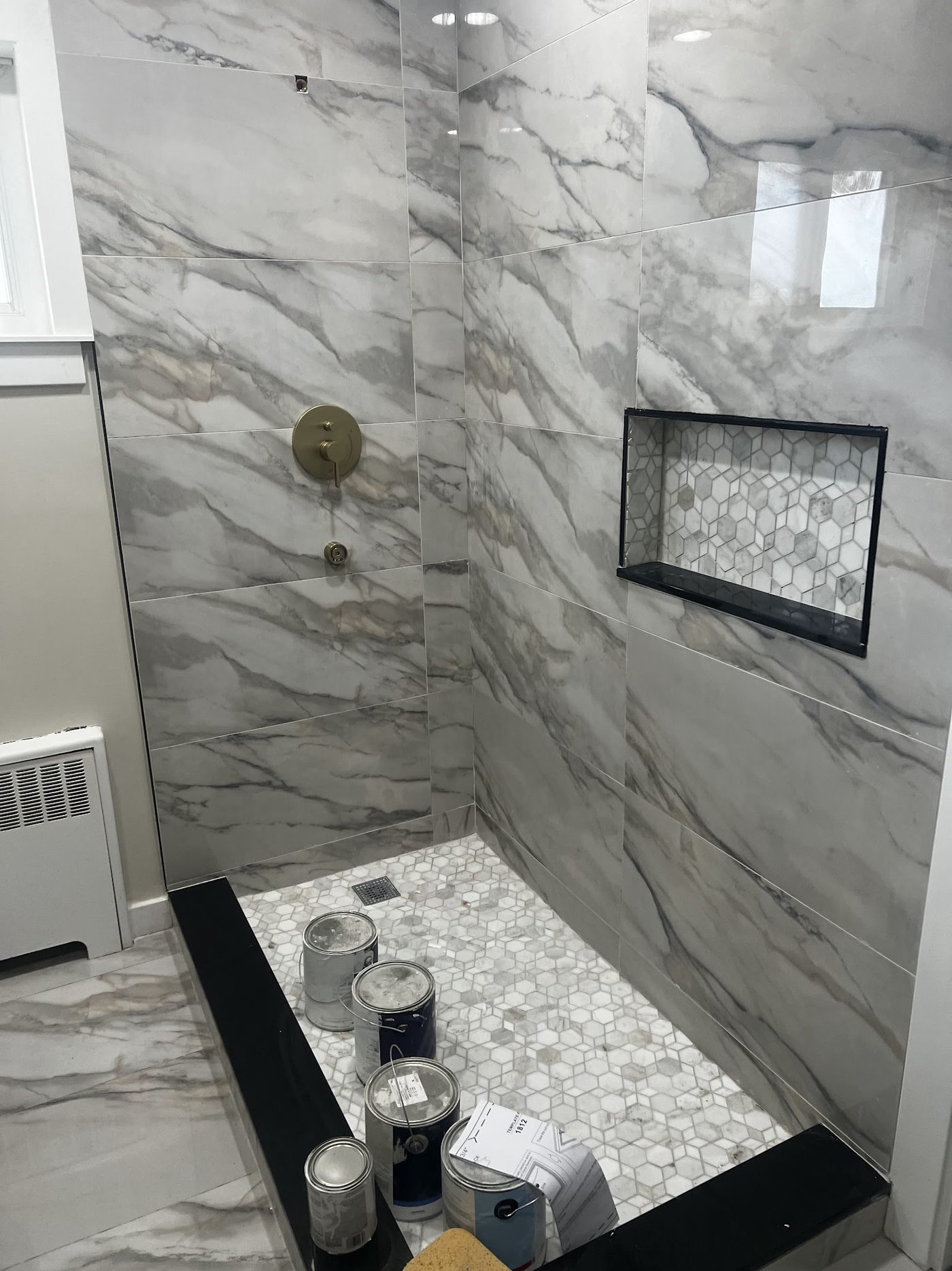 A shower tiled floor to ceiling in marble-look porcelain with a hexagon mosaic niche and brushed gold fixtures.