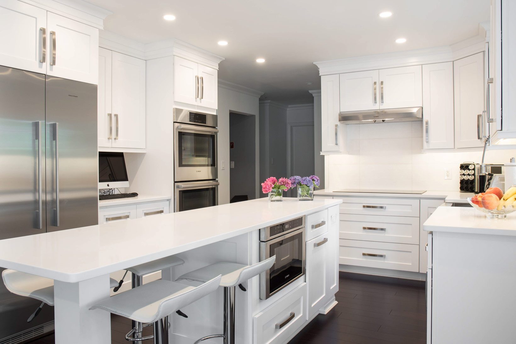 A white shaker kitchen with a long quartz island, double ovens and stainless appliances, built by Amazing Kitchen and Bath.