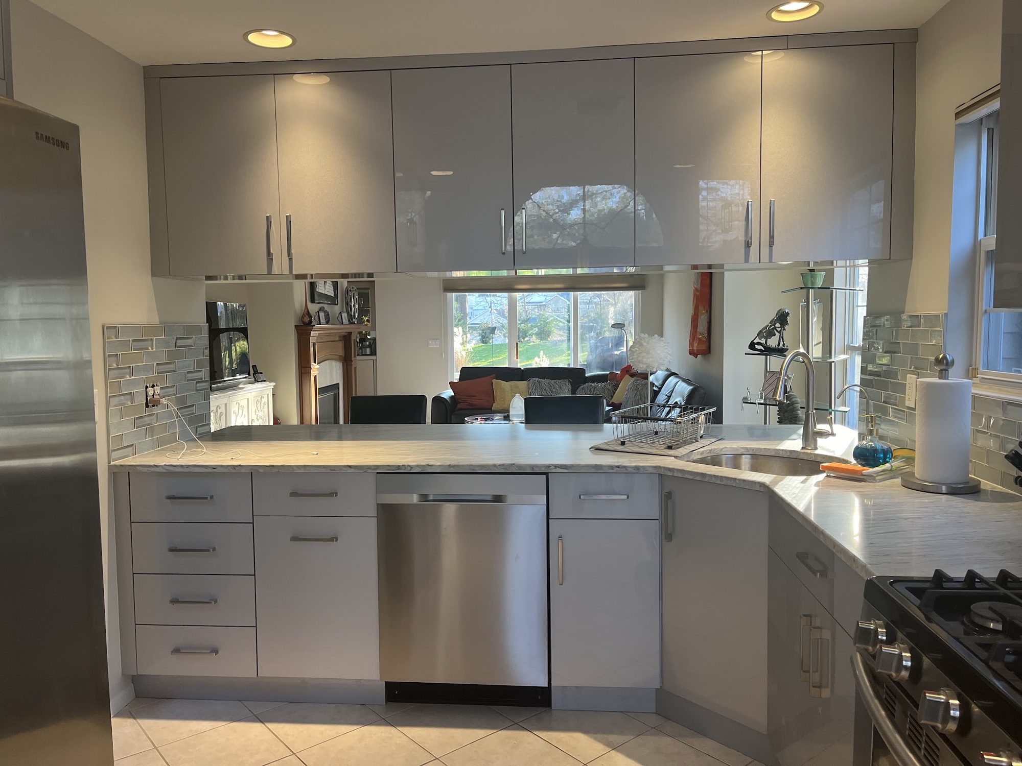 A high-gloss grey kitchen with a marble-veined countertop, glass tile backsplash and stainless appliances.